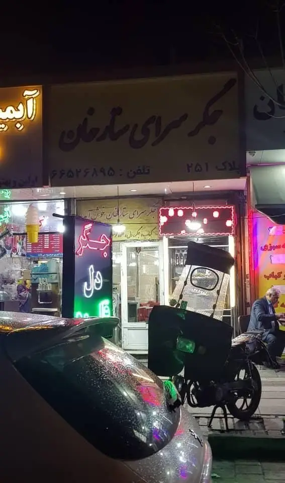 جگرسرای ستارخان، رستوران پرطرفدار کباب جگر و دل در تهران، نمای شب با تابلوهای روشن، تلفن ۶۶۵۲۶۸۹۵ و موتور تحویل غذا.