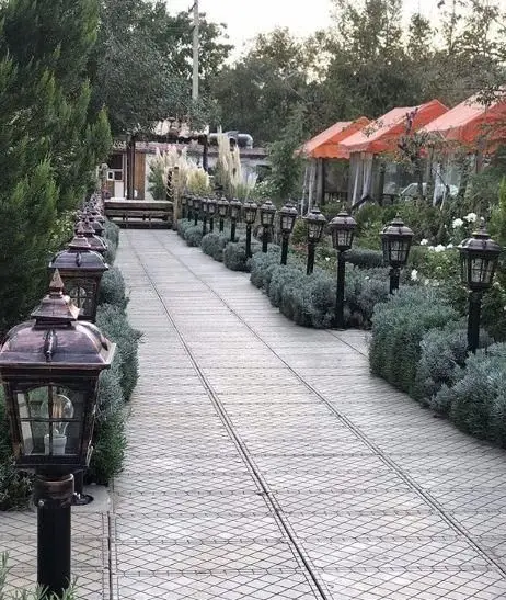 مسیر نورپردازی شده و فضای سبز دلنشین سفره خانه سنتی چهل ستون با آلاچیق‌های نارنجی و درختان بلند برای تجربه غذایی لذت‌بخش.