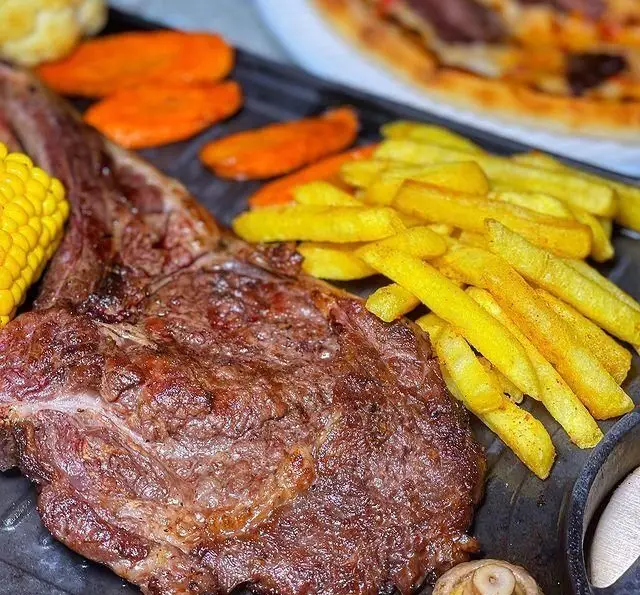 استیک تاماهاک آبدار و لذیذ همراه با سیب زمینی سرخ کرده طلایی، ذرت و هویج تازه در کافه رستوران دریا باز. یک انتخاب عالی برای شام.