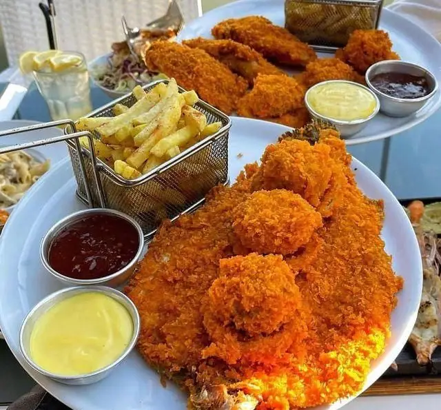 نمایی اشتهاآور از بشقاب پر فیله سوخاری کریسپی، سیب زمینی سرخ کرده طلایی و سس‌های لذیذ در کافه رستوران دریا باز