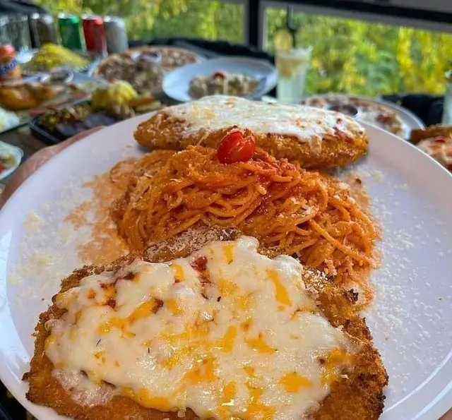 تصویری دلنشین از شنیتسل پنیری و پاستا در کافه رستوران دریا باز، میز پر از غذاهای متنوع با منظره‌ای زیبا و چشم‌نواز.