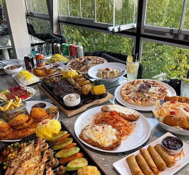 تجربه طعم‌های بی‌نظیر در کافه رستوران دریا باز. میزی پر از استیک، پیتزا، پاستا، میگو، جوجه و غذاهای فرنگی و ایرانی متنوع در فضایی دلنشین.