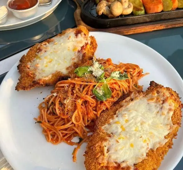 چیکن پارمژان خوشمزه با اسپاگتی سس قرمز و پنیر ذوب شده در کافه رستوران دریا باز، یک غذای ایتالیایی عالی برای ناهار یا شام.