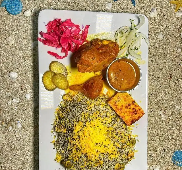 غذای خوشمزه و زیبای ایرانی از کافه رستوران دریا باز شامل پلو زعفرانی و سبزی، مرغ، به همراه مخلفات متنوع و اشتهاآور.