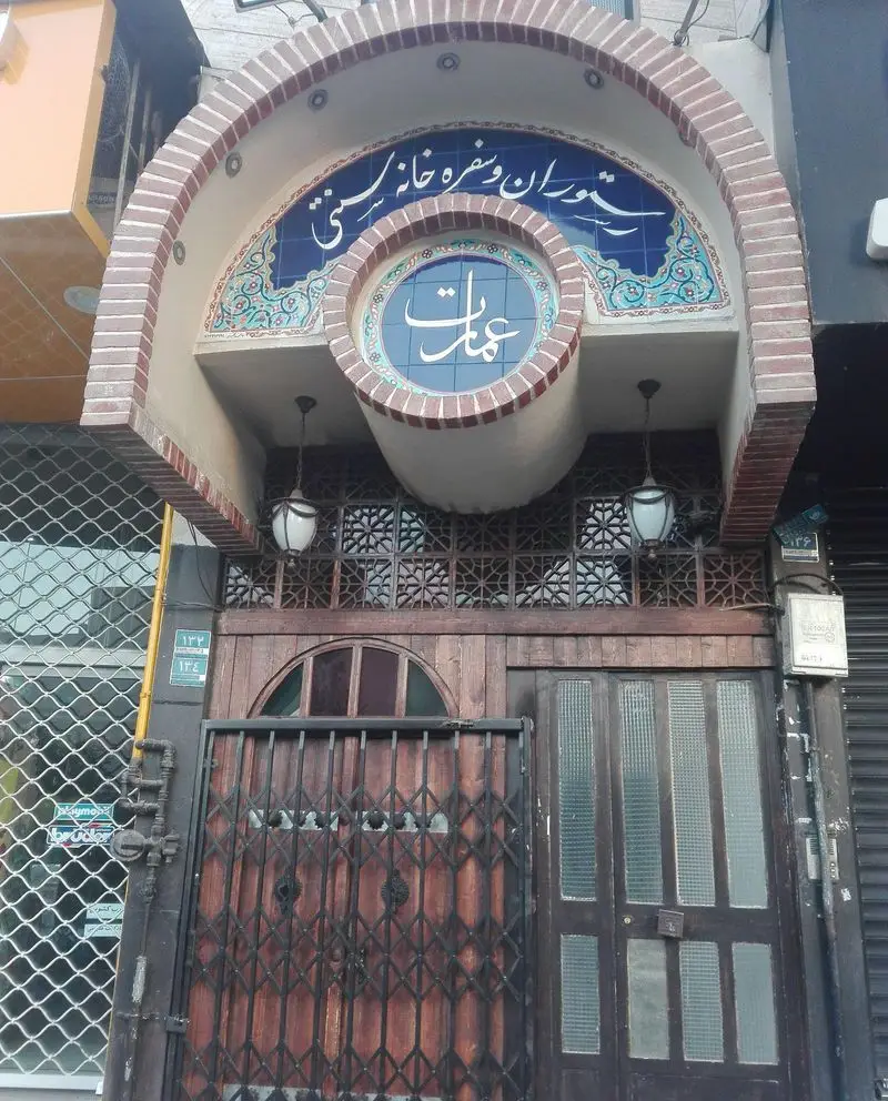 تصویر نمای ورودی رستوران و سفره خانه سنتی عمارت با کاشی‌کاری آبی زیبا، درب چوبی سنتی و گیت فلزی محافظ. فضایی اصیل.