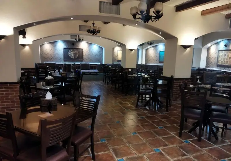 نمایی از فضای داخلی آرام و دلنشین رستوران سنتی عمارت با چیدمان منظم میز و صندلی‌های چوبی، دکوراسیون کلاسیک و دیوارهای آجری.