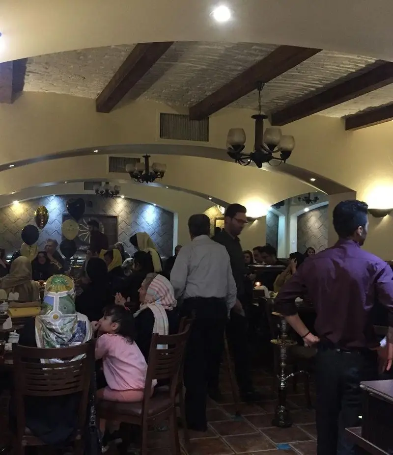 رستوران سنتی عمارت: محیطی دلنشین با دکوراسیون ایرانی، میهمانان در حال صرف غذای سنتی و قلیان در فضایی گرم و خانوادگی.