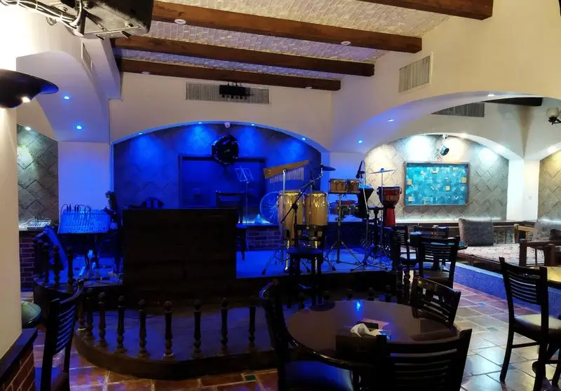 فضای دلنشین و داخلی رستوران سنتی عمارت با استیج موسیقی زنده، نورپردازی خاص آبی و چیدمان کلاسیک میز و صندلی‌ها.