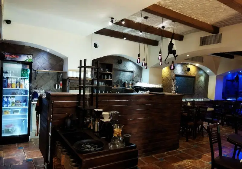 فضای داخلی رستوران سنتی عمارت با دکوراسیون چوبی، پیشخوان قهوه، نورپردازی گرم، میز و صندلی‌های شیک و محیطی دنج برای مشتریان.