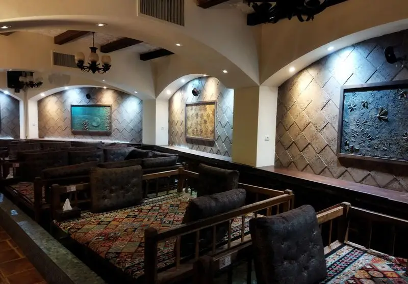 رستوران سنتی عمارت: نمایی از فضای داخلی دلپذیر با تخت‌های سنتی، فرش‌های ایرانی، دیوارپوش‌های بافت‌دار و نورپردازی جذاب برای مهمانان.