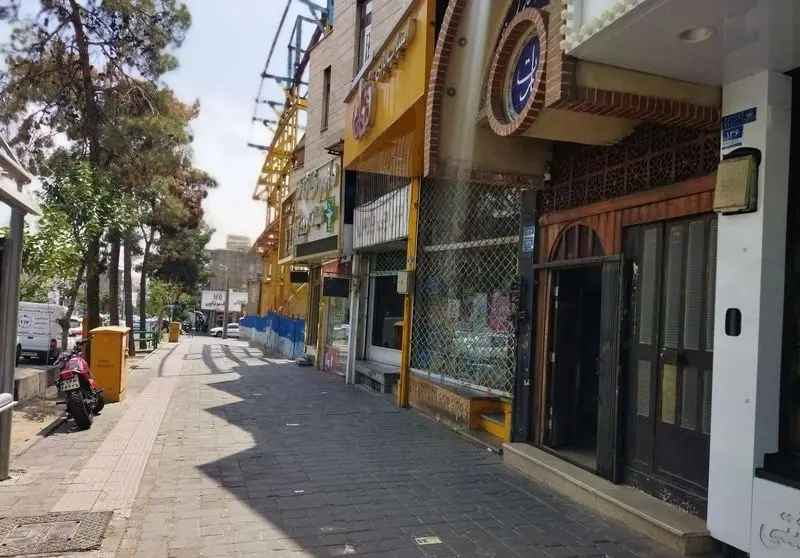 نمای خارجی رستوران سنتی عمارت، ساختمان زردرنگ آن در خیابانی با درختان بلند و دیگر فروشگاه‌ها، محیطی دلپذیر برای مشتریان.