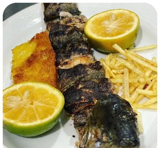 کباب ماهی خوشمزه رستوران سید شهرری با ته دیگ زعفرانی، سیب زمینی سرخ کرده و لیمو تازه. غذای دریایی لذیذ و دلپذیر.