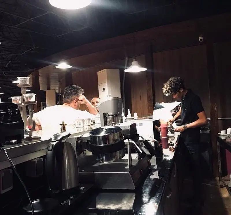 باریستا با مهارت نوشیدنی و دسر وافل را در کافه رستوران پرشین گلف آماده می‌کند. مشتریان از فضای گرم و دلنشین لذت می‌برند.