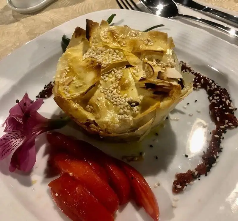 تصویری جذاب از بشقاب ویژه رستوران پرشین گلف: پای فیلو کنجدی با دیزاین گل، فلفل قرمز و سس خاص. طعم‌های اصیل ایرانی.