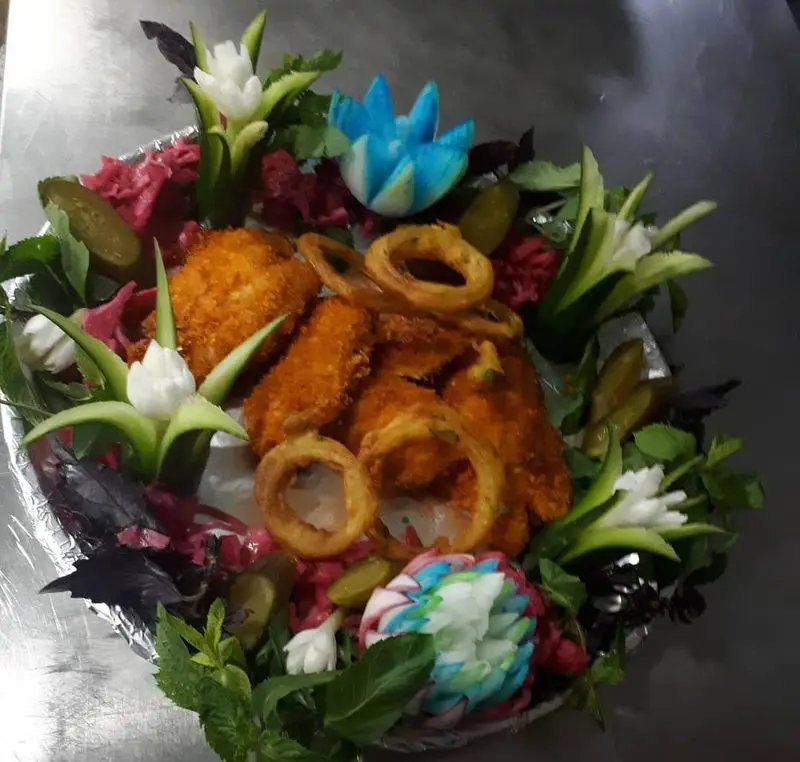 سینی مرغ و پیاز سوخاری ترد و لذیذ رستوران پرشین گلف، با تزئینات هنرمندانه سبزیجات، گل‌های رنگی و چاشنی‌های تازه و خوش‌طعم.