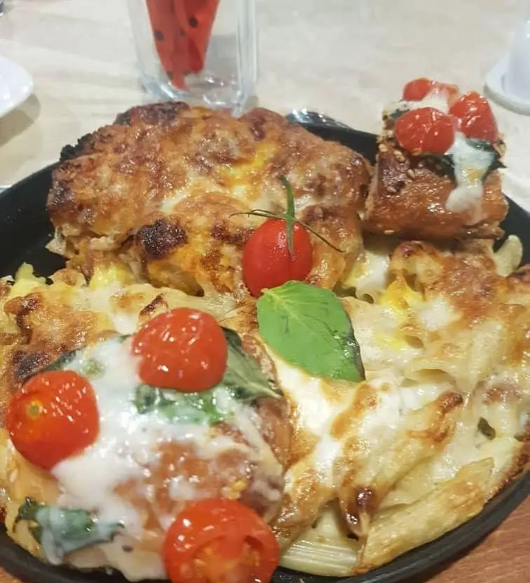 پاستا پخته شده گراتن با لایه‌ای از پنیر ذوب شده و طلایی، تزئین شده با گوجه گیلاسی و ریحان، مخصوص رستوران پرشین گلف.