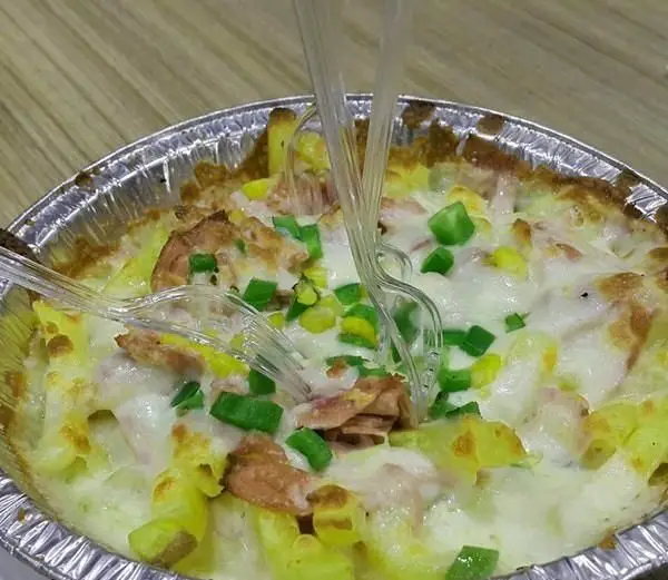 تصویری از ماکارونی پنیری طلایی و لذیذ پیتزا میلان، حاوی تکه‌های مرغ، فلفل دلمه‌ای سبز و ذرت، سرو شده در ظرف یکبار مصرف با چنگال.