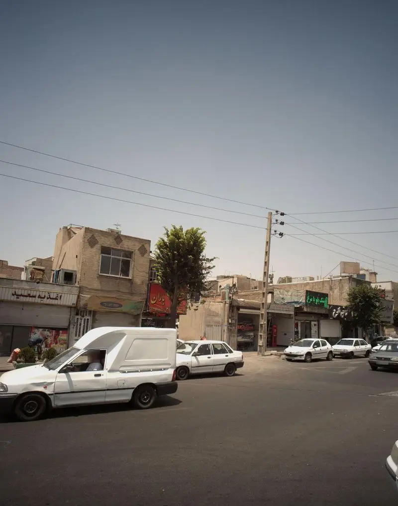 تصویری از خیابان شلوغ و کسب و کارهای محلی در یک شهر ایرانی. تابلوی اغذیه سعید به وضوح دیده می‌شود، با خودروها و یک آسمان صاف.