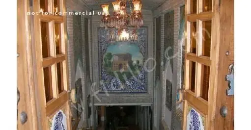 ورودی لوکس رستوران سنتی عالی قاپو با درب‌های چوبی منبت‌کاری شده، لوستر کریستالی و کاشی‌کاری‌های زیبای ایرانی.