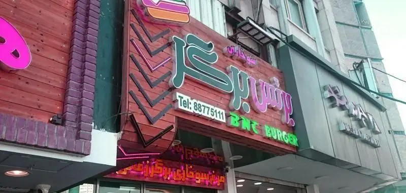 تصویر نمای بیرونی فست فود برنس برگر (BNT BURGER) با لوگوی همبرگر، شماره تماس 88775111 و تابلوی درخشان.