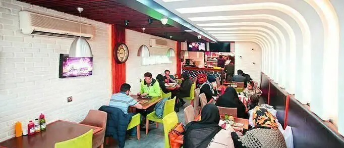 فضای داخلی پر جنب و جوش برنس برگر، فست فودی مدرن با دکوراسیون جذاب، دیوارهای آجری سفید و مشتریان مشغول صرف غذاهای لذیذ.