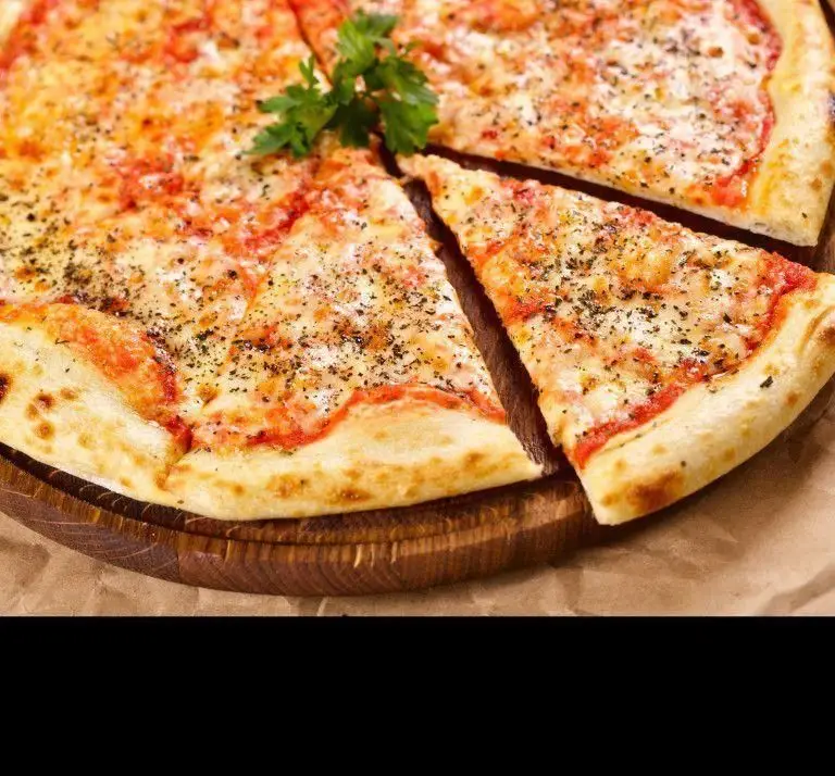 پیتزا مارگاریتا کلاسیک و تازه کافه فست فود لیوادو، با پنیر آب شده، سس گوجه و سبزیجات معطر روی میز چوبی.