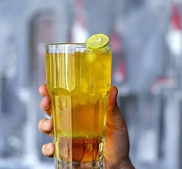 یک لیوان نوشیدنی خنک لایه‌دار با یخ و برش لیمو تازه در دست، نمایی از نوشیدنی‌های گوارا در كافه رستوران پلاك ٥.
