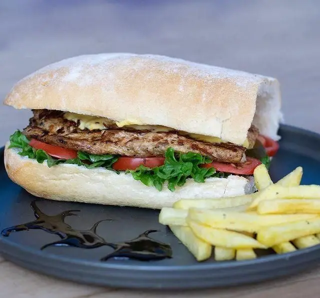 ساندویچ مرغ گریل با نان چاباتا، کاهو، گوجه و سس زرد، همراه سیب زمینی سرخ کرده، در کافه رستوران پلاک ٥. یک وعده غذای لذیذ.