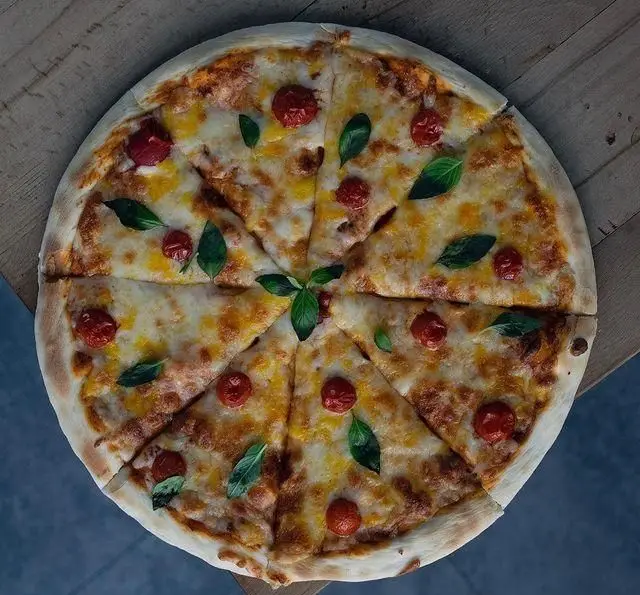 پیتزا مارگاریتای تازه و خوشمزه با پنیر، گوجه گیلاسی و برگ ریحان از کافه رستوران پلاک ٥. ایده‌آل برای تجربه‌ی غذای ایتالیایی.