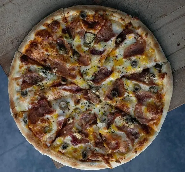 تصویری از پیتزای خوشمزه و داغ پلاک ٥ با ژامبون و زیتون، آماده سرو در محیطی جذاب. لذت طعم اصیل ایتالیایی را در کافه رستوران ما تجربه کنید.