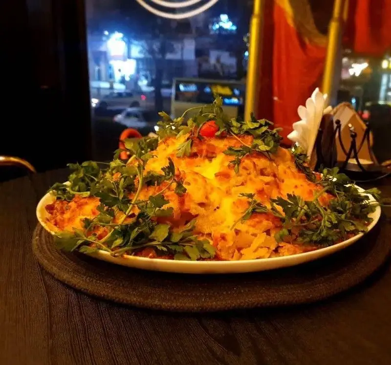 غذای ویژه کافه ویترای: یک ظرف بزرگ و خوش‌رنگ از غذای پنیری با سیب‌زمینی و سبزیجات تازه در محیط دنج کافه.