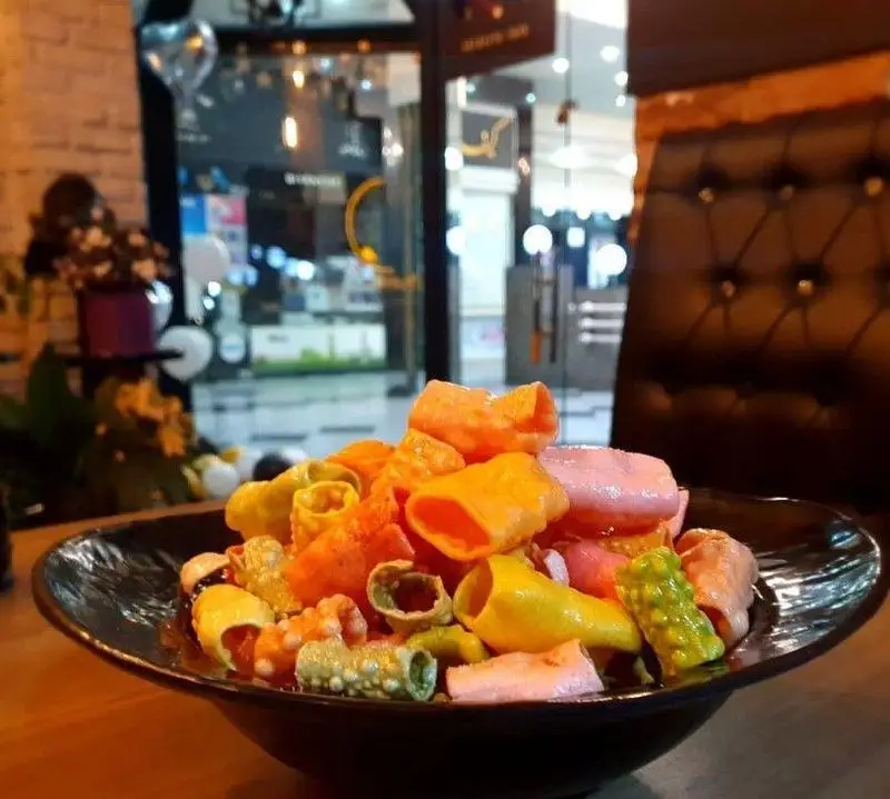 تصویری از کاسه‌ای پر از چیپس و اسنک‌های رنگارنگ و متنوع بر روی میز چوبی کافه ویترای، نشانگر فضای دلنشین و تنقلات خوشمزه.