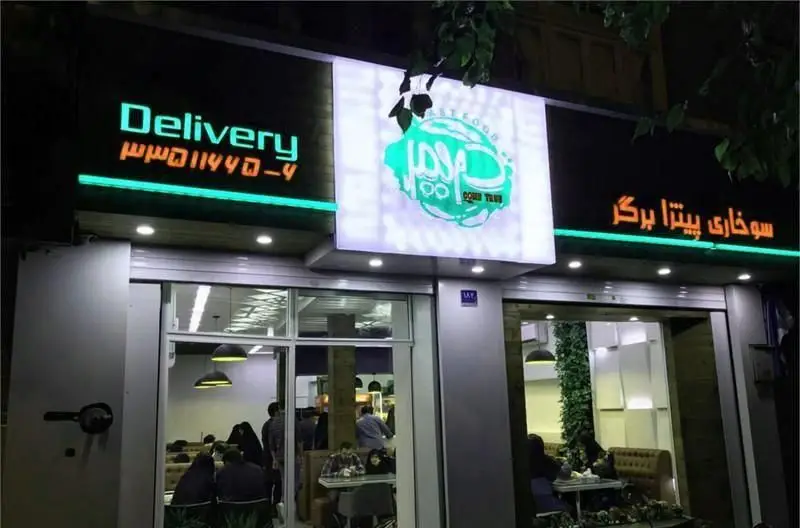 تصویر نمای بیرونی فست فود دریم در شب با تابلوی روشن Delivery و شماره تماس ۰-۴۴۰۱۱۴۴۰. انواع سوخاری، پیتزا و برگر برای سفارش آنلاین و حضوری.
