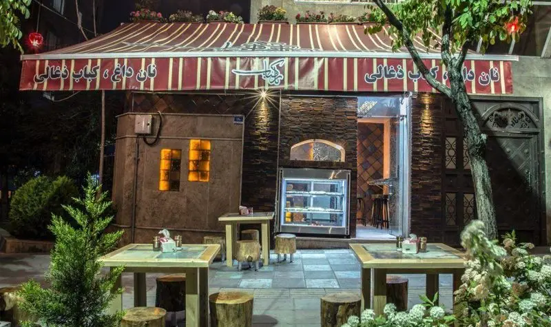 نمای بیرونی رستوران نارکباب در شب با فضای باز دلنشین، میزهای چوبی و سایبان راه راه، همراه با نان داغ و کباب ذغالی.