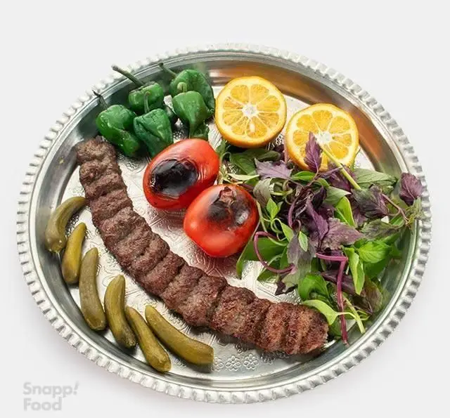 یک سیخ کباب کوبیده معروف رستوران نارکباب با گوجه و فلفل کبابی، سبزی معطر، لیموترش و خیارشور روی سینی شیک
