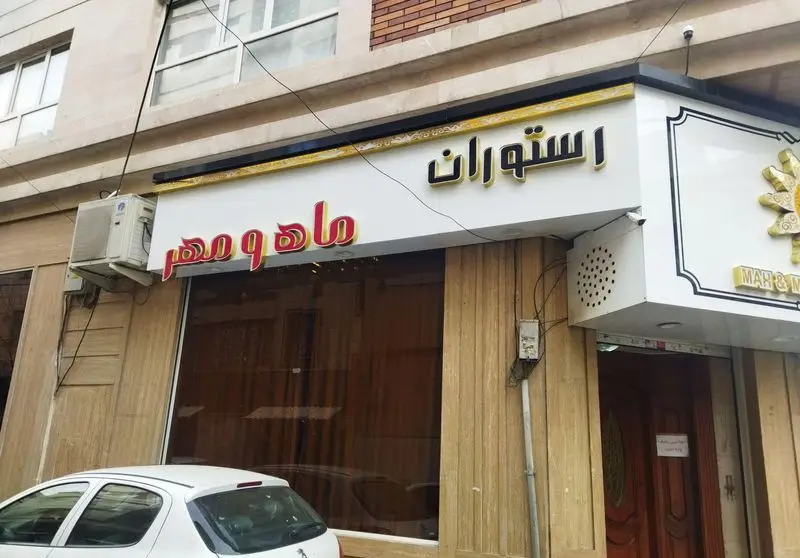 تصویر نمای بیرونی رستوران ماه و مهر با تابلوی چشم‌نواز فارسی و انگلیسی، منتظر مهمانان برای تجربه غذایی دلپذیر.