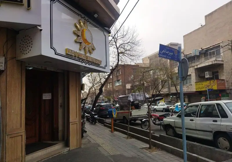 نمای بیرونی رستوران ماه و مهر با تابلوی خورشید و ماه، در کنار خیابان میرصانعی، با پیاده‌رو و خودروهای پارک شده.