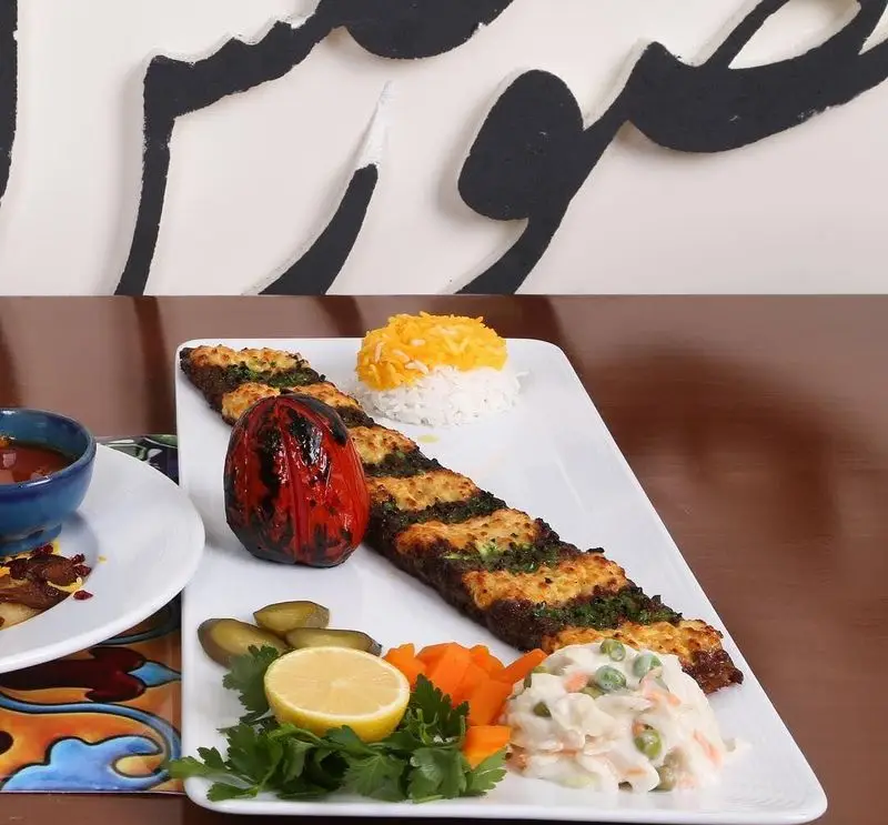 نمایی از یک پرس کباب اصیل ایرانی با برنج زعفرانی، گوجه کبابی و سالاد، در فضای دلنشین رستوران سنتی خوان کرم.