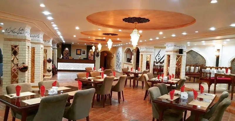 فضای داخلی رستوران سنتی خوان کرم با ستون‌های آجری، لوسترهای آویز و خوشنویسی فارسی، محیطی دلنشین برای صرف غذای ایرانی.