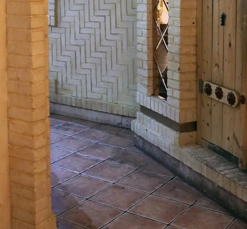 نمایی از فضای داخلی رستوران سنتی خوان کرم با معماری خاص شامل دیوارهای آجری با طرح جناغی، در چوبی سنتی و کفپوش کاشی.