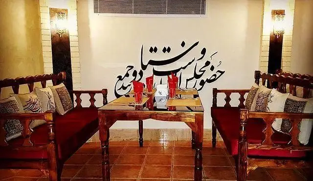 نمایی از فضای داخلی رستوران سنتی خوان کرم با دکوراسیون سنتی، میز و صندلی چوبی، و نقاشی خط فارسی روی دیوار. مکانی دنج و دلنشین.