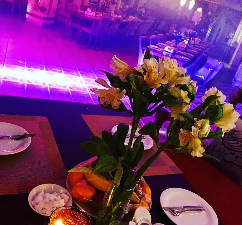 فضای داخلی زیبای رستوران سنتی خوان کرم، میزی چیده شده با گل و نورپردازی بنفش، محیطی دلنشین برای صرف غذا و دورهمی.