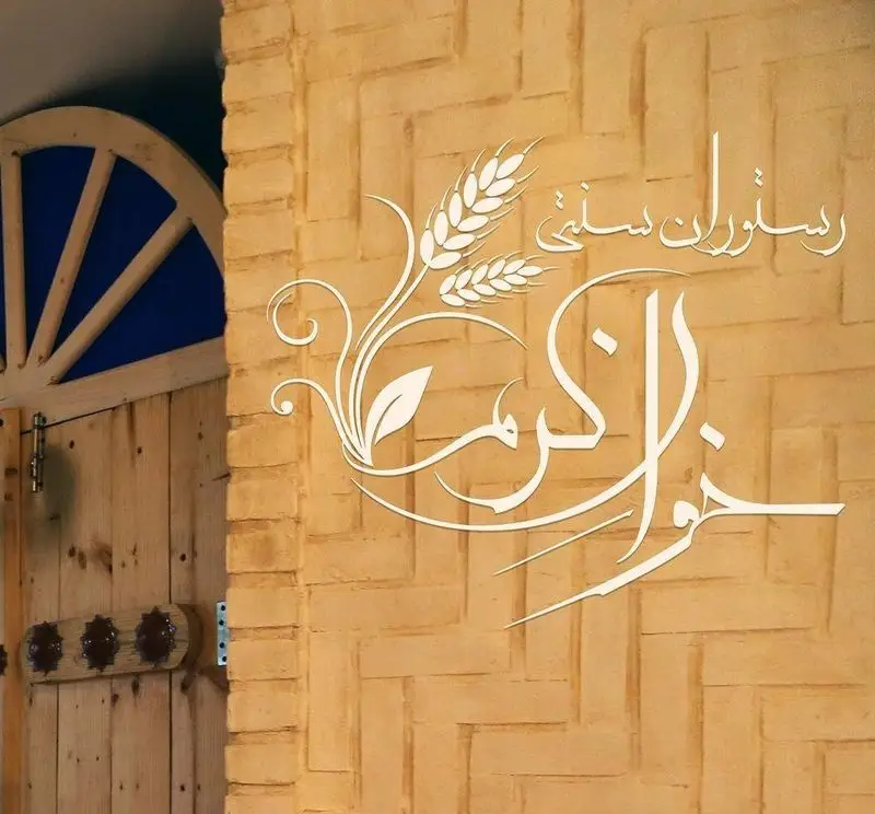 لوگوی خوان کرم، رستوران سنتی معروف، بر روی دیوار آجری قدیمی با نقوش گندم. ورودی جذاب با درب چوبی سنتی و پنجره آبی، فضای دلنشین.