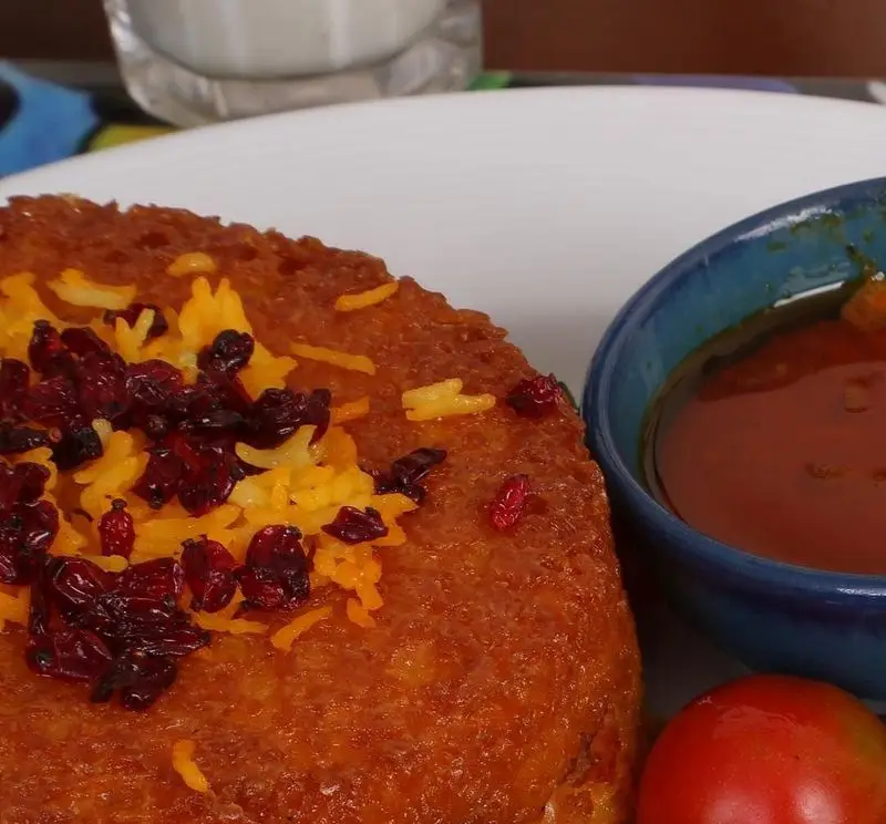 غذای سنتی ایرانی: ته دیگ زعفرانی برشته با زرشک و پلو زعفرانی در کنار خورشت و گوجه فرنگی. منویی لذیذ از رستوران خوان کرم.