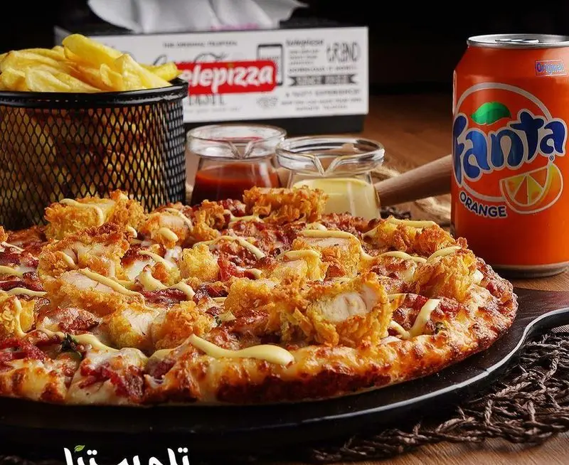 پیتزا کریسپی چیکن خوشمزه و داغ تله پیتزا به همراه سیب‌زمینی سرخ‌شده ترد و نوشابه فانتا نارنجی، یک وعده کامل و لذیذ فست فود.