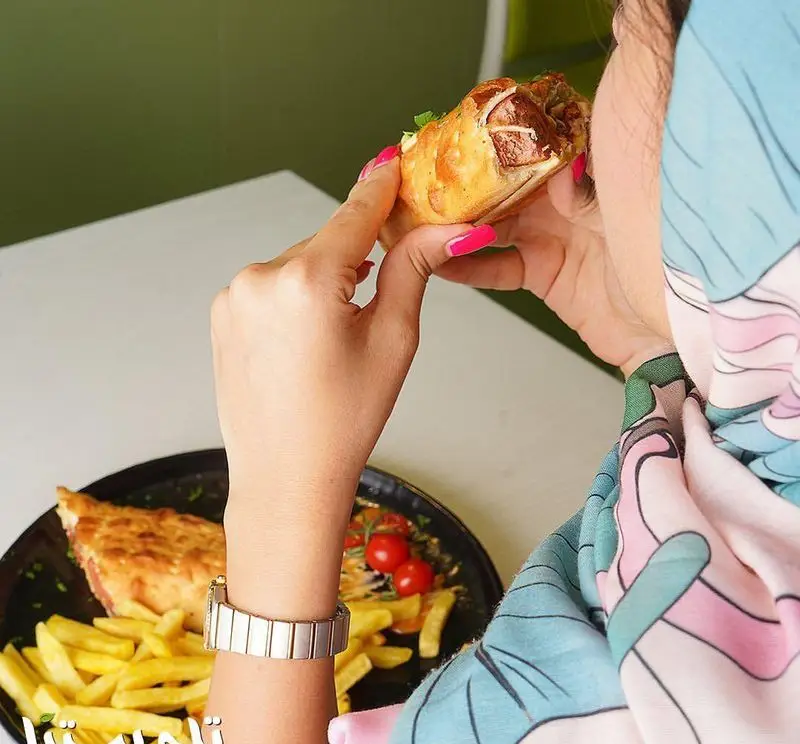 تصویری از مشتری در فست فود تله پیتزا: لذت بردن از ساندویچ رول داغ و کریسپی به همراه سیب زمینی سرخ کرده تازه و پیتزای لذیذ.