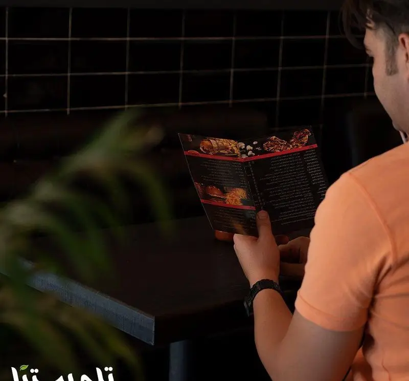 مشتری در فست فود تله پیتزا در حال مطالعه دقیق منوی غذاها. انتخاب غذای مورد علاقه از منوی متنوع و جذاب تله پیتزا.