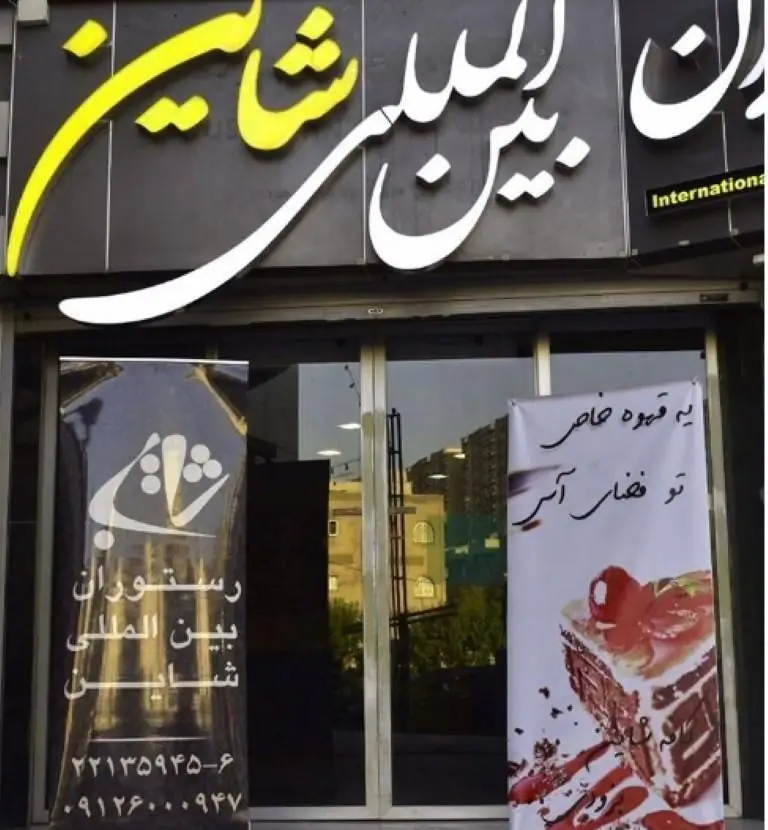 رستوران بین المللی شاین، نمای بیرونی با تابلوی بزرگ، لوگوی خاص، بنرهای تبلیغاتی قهوه و کیک، و شماره‌های تماس برای رزرو.