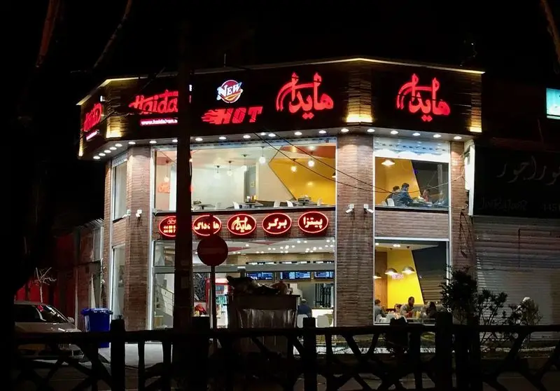 نمای خارجی پرنور فست فود هایدا در شب، با تابلوهای نئونی Haida، New HOT و منوی پیتزا، برگر و هات داگ.