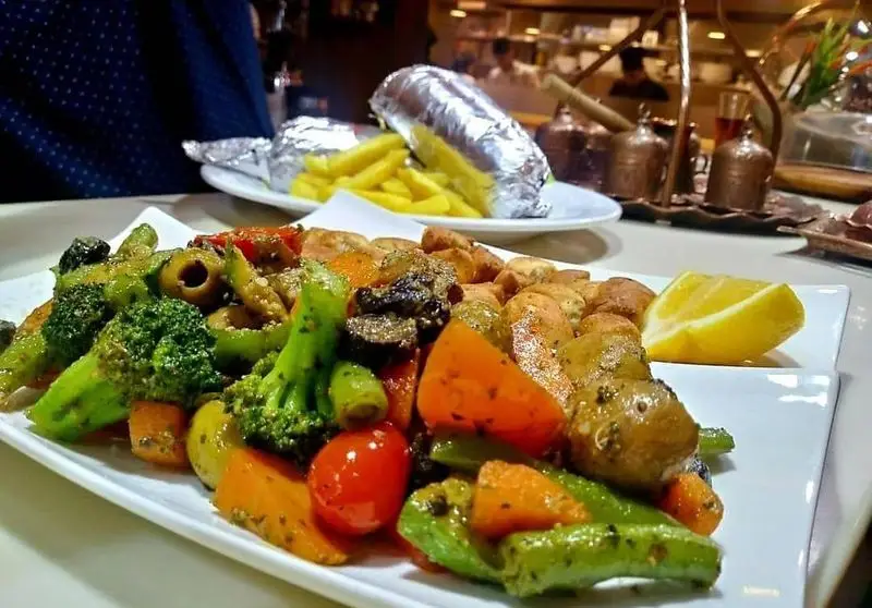 یک بشقاب غذای لذیذ شامل سبزیجات کبابی و سیب‌زمینی‌های کوچک به همراه لیمو در رستوران ایتالیایی رو ب رو، انتخابی سالم برای ناهار یا شام.